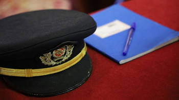 A hat from the Military Uniform of the Fire Brigade, and a blue notebook are placed on a red bench